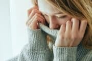 A woman in a grey knit sweater pulls the collar up to partially cover her face, representing the internal struggle of generalized anxiety disorder.