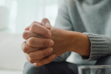 Person with clasped hands during an online therapy session.