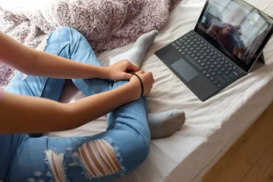 Young person sitting on a bed during an online therapy session on a laptop.