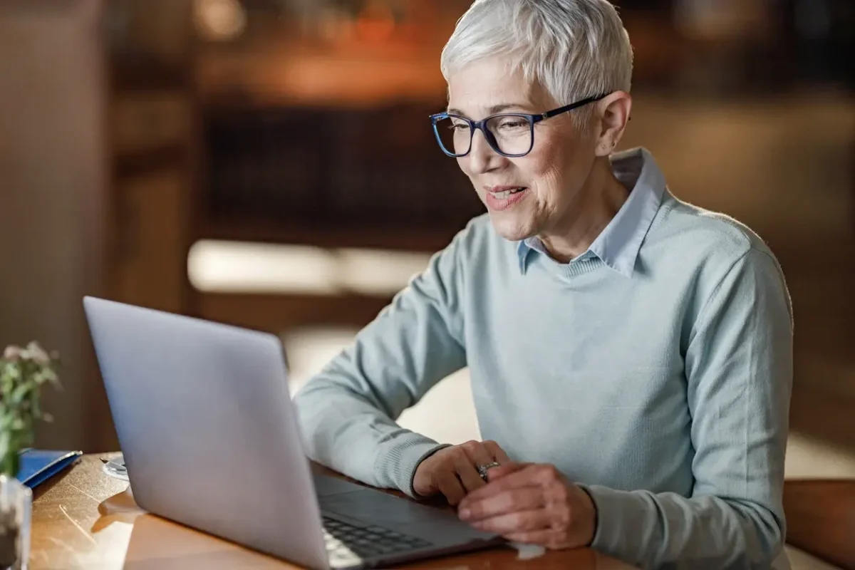 Older woman smiling while using a laptop during an online therapy session at home.