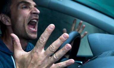 Angry man at steering wheel of car, hands off wheel and gesturing as he yells