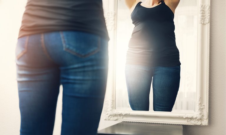 Woman obsessing over body fat in the mirror