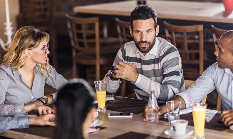 Business colleagues around restaurant table conversing, beverages served