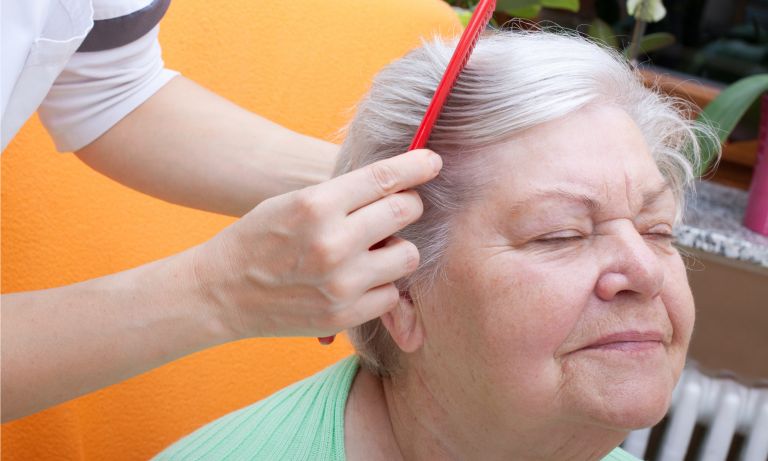 Caretaker combing hair of contented senior woman