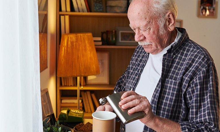Elderly man adding alcohol to his mug of tea