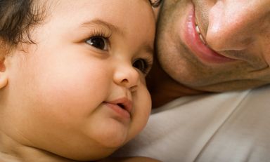 Secure infant gazes out, relaxed, as he's cradled by his smiling father