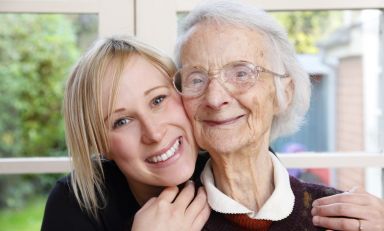 Young woman gently holds older one, the two of them cheek to cheek, both smiling