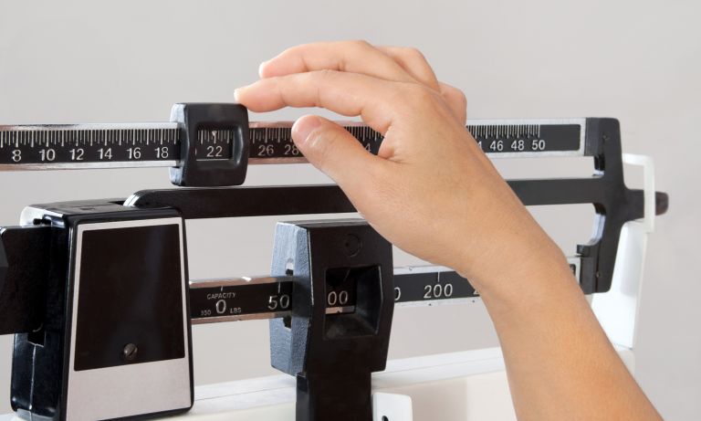 Hand sliding the counterweight at the top of a physician's beam scale