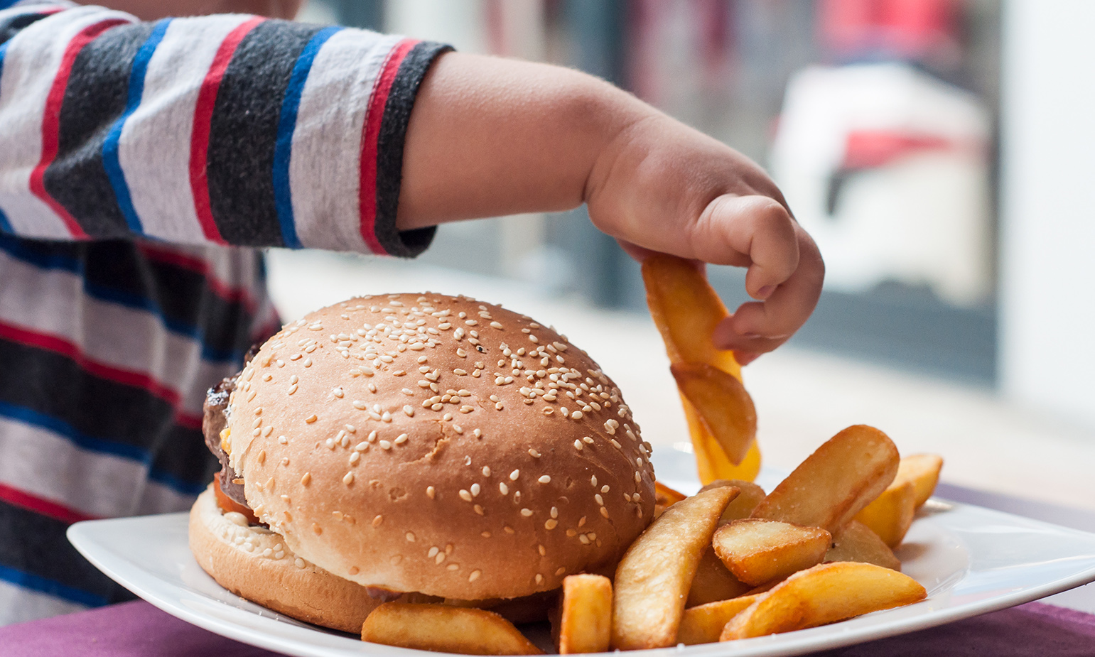 Child grabbing from a stack of large french fry wedges on plate with adult-sized hamburger