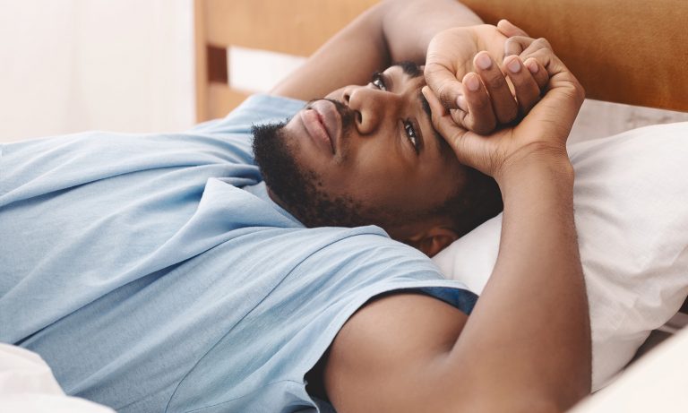 Man lying in bed, eyes open, suffering from insomnia sleep disorder