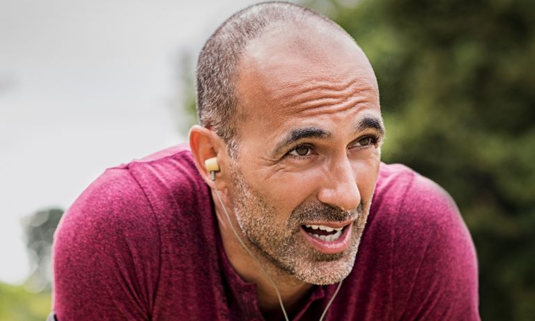 Closeup of man pausing during outdoor running session, earbuds in ears, leaning forward, chin up, looking forward intensely