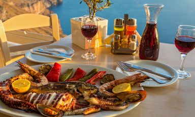 Mediterranean meal on platter with table setting, ocean overlook, seafood, vegetables, red wine served from carafe, olive oil