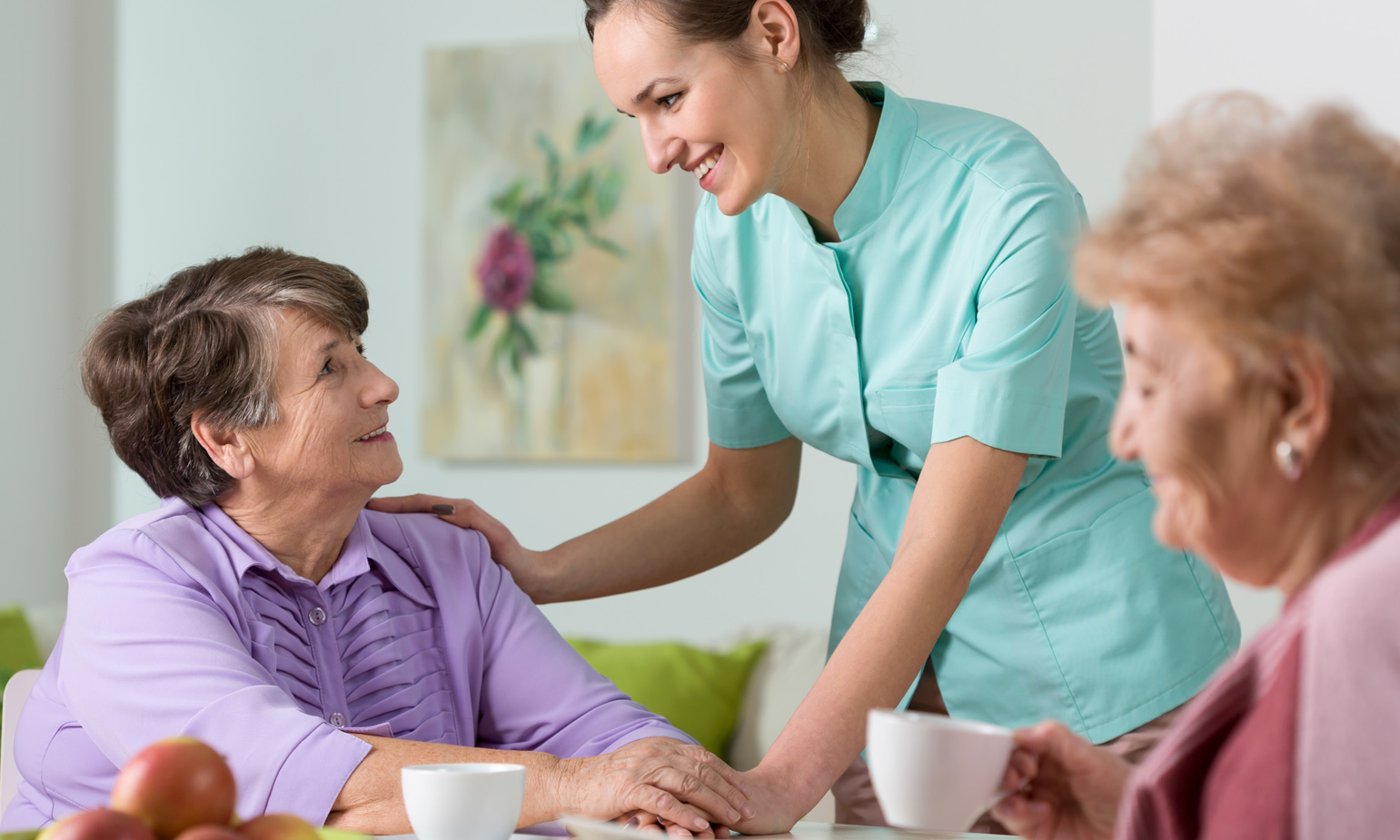 Caring nurse smiling with older lady seated in dining area