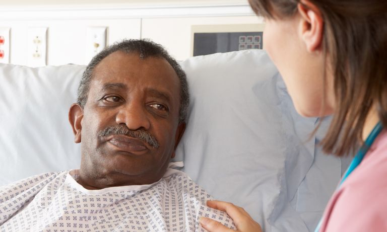 Nurse talking to senior male patient laying on bed in inpatient care unit