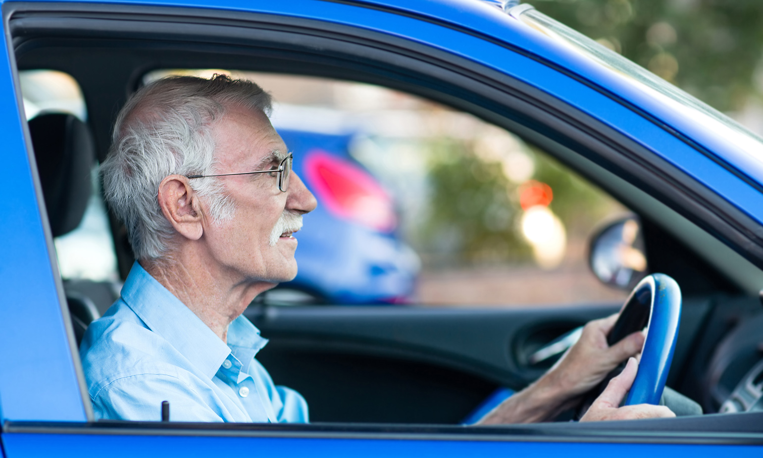 Profile view through open passenger window of older man clutching steering wheel of car