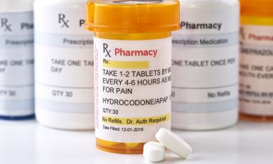 Prescription pill bottle containing hydrocodone tablets in front of other pill bottles