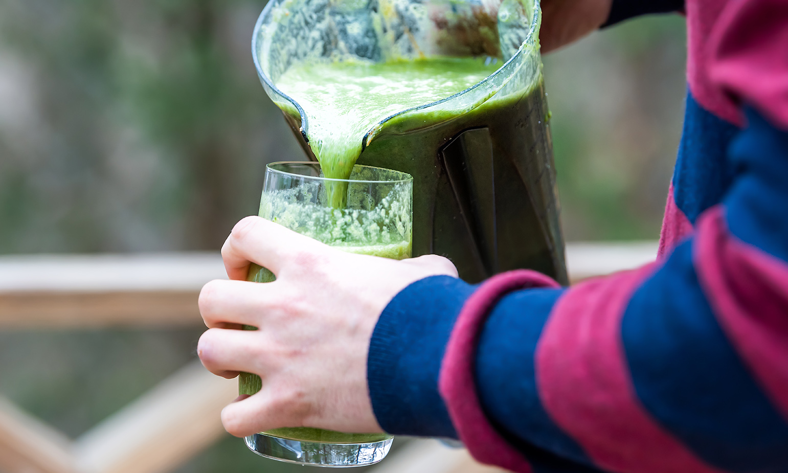 Person pouring healthy green drink from pitcher into glass