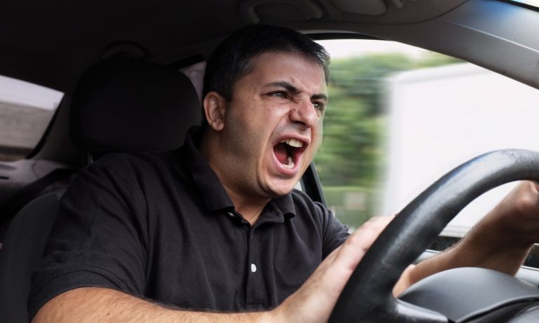 Man seated behind steering wheel, honking his horn and yelling in anger