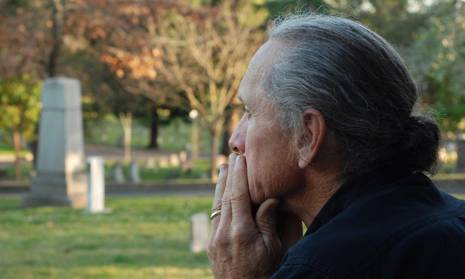 Bereaved, grief-stricken man in foreground, gravestones in the distance