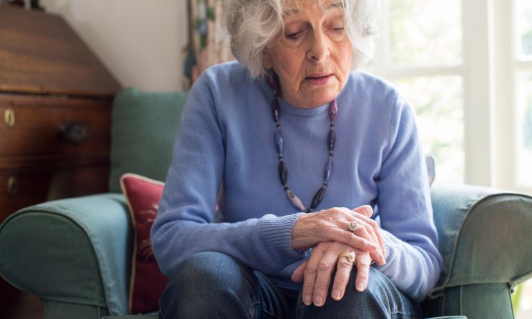 starsza kobieta siedząca w tapicerowanym fotelu, kładąca jedną rękę na drugiej spoczywająca na kolanie, nie w pełni czujna