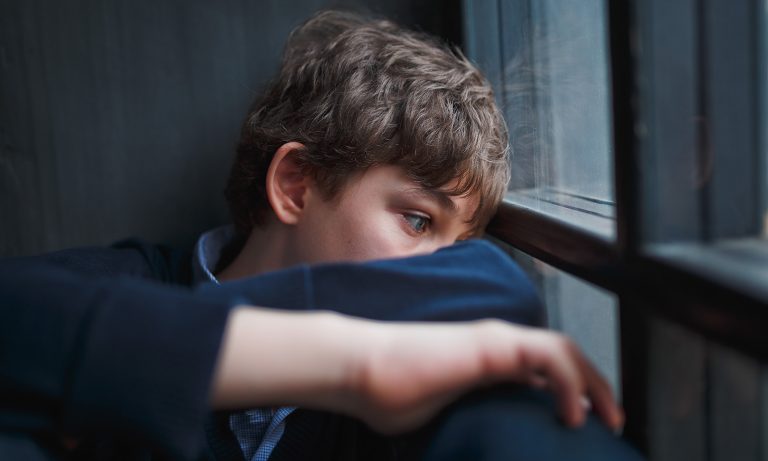 Teenaged boy curled up inside window, face against arm, eyes wide