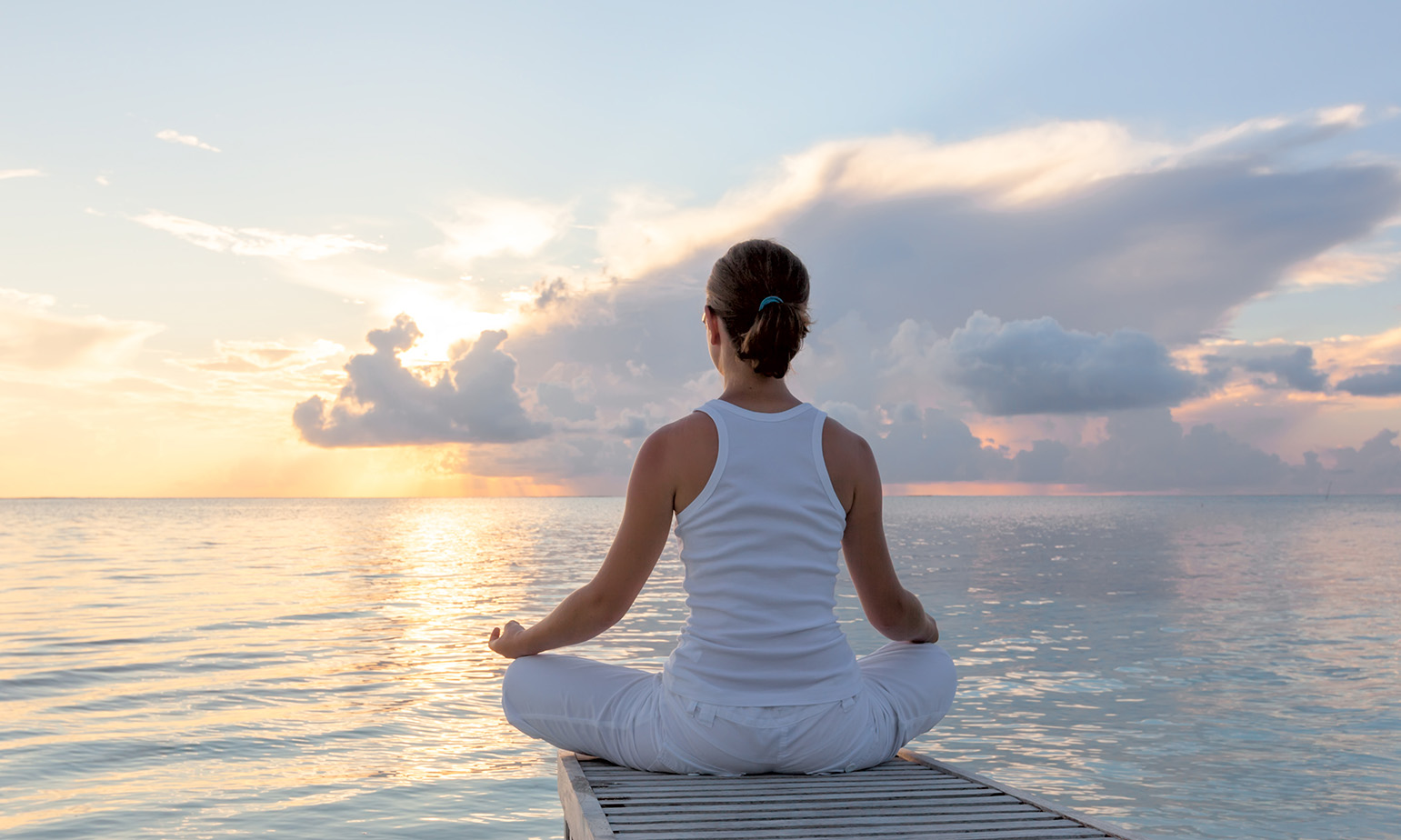 Woman at edge of dock, sitting in lotus position