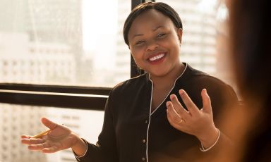 Woman smiling while communicating in office tower conference room, a view of other high rise buildings behind her