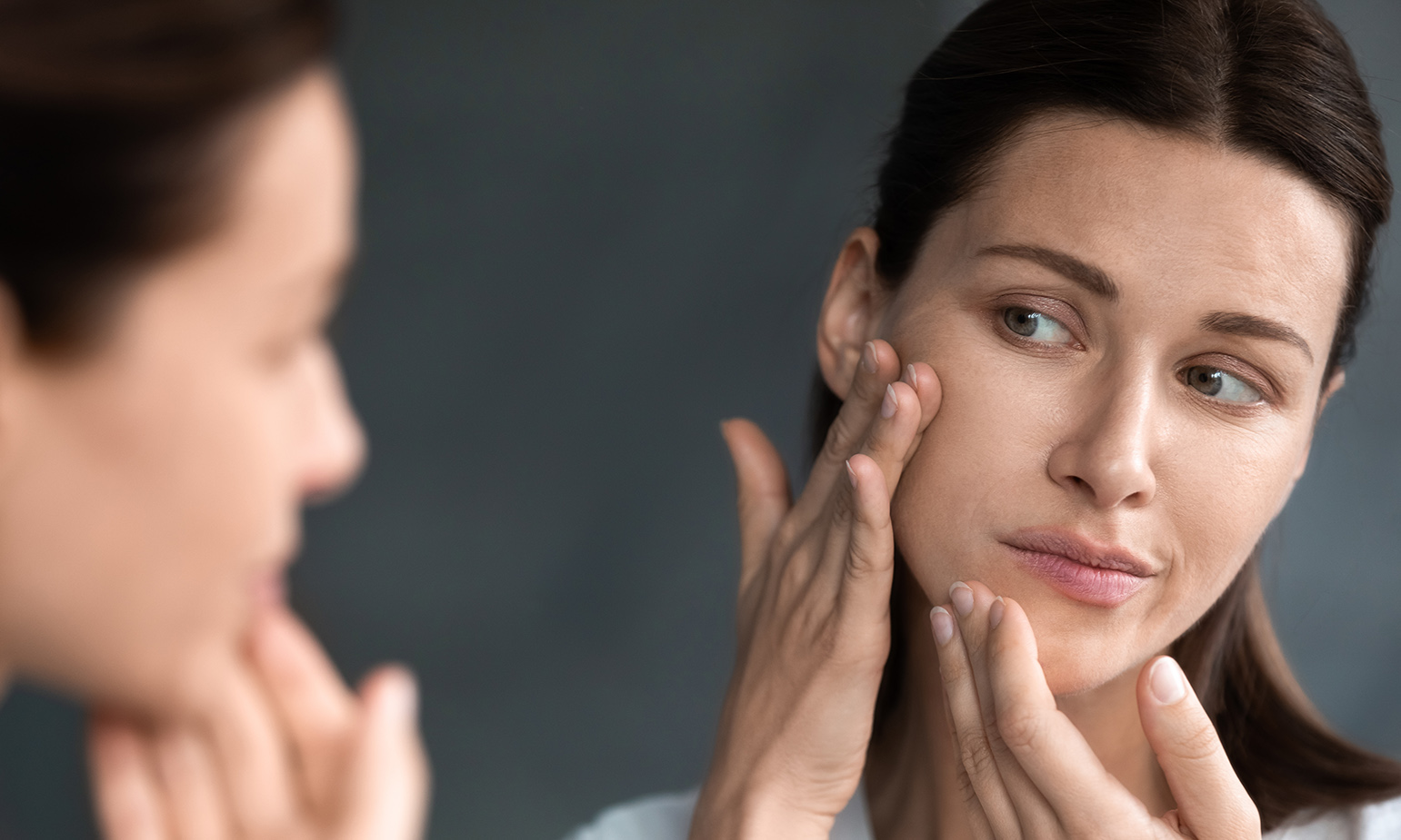 Woman examining face in mirror unhappy