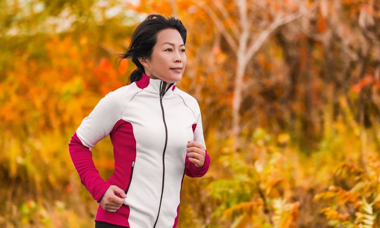 Woman in fleece jacket jogs with colorful autumn leaves in background