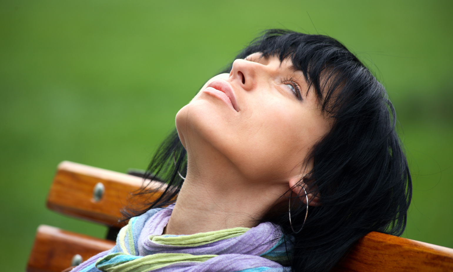 Closeup of woman sitting on park bench, head leaning back against backrest, lost in thought