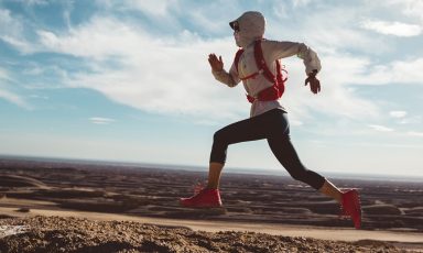 Woman, bandana over her face, runs along dirt trail in arid landscape