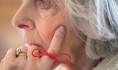 Elderly woman, hand on side of face, reminder string tied in bow on finger