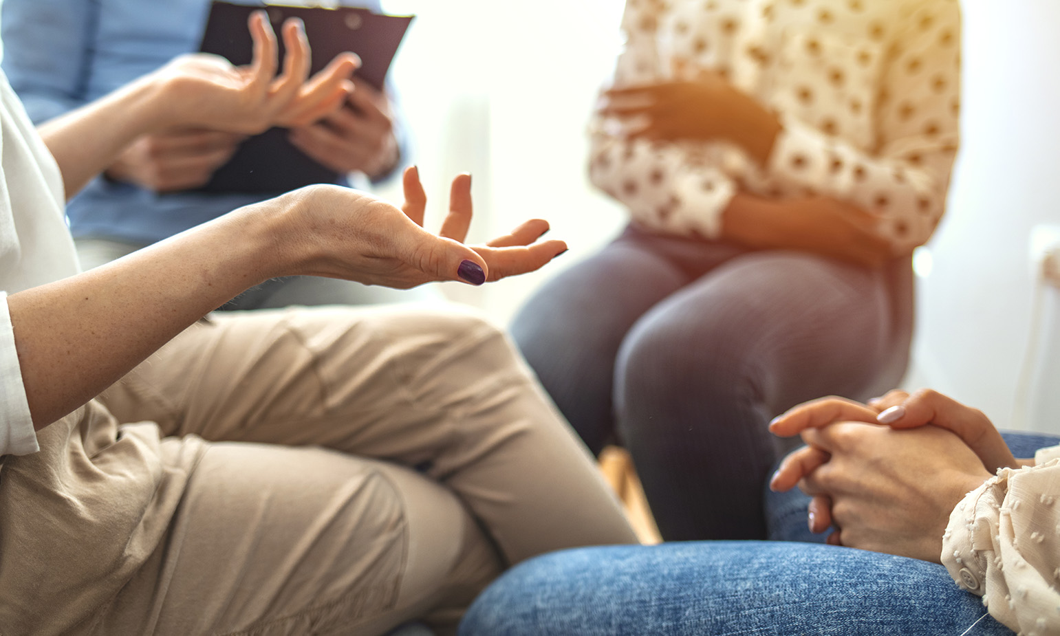 Woman's hands gesturing in small group sitting in circle, one person with clipboard, group therapy, support