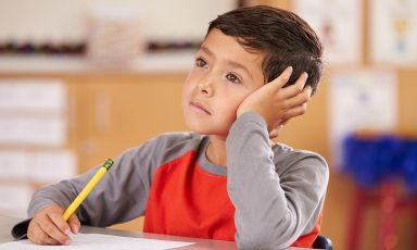 Young boy at school desk staring into space