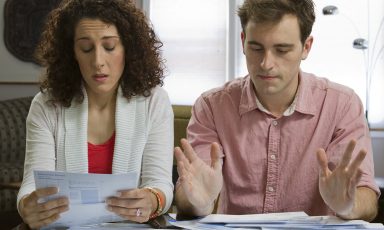 Young couple at table at home reviewing their personal financials, woman concerned, man fed up