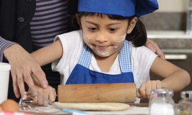 Young girl in bakers hat rolls dough
