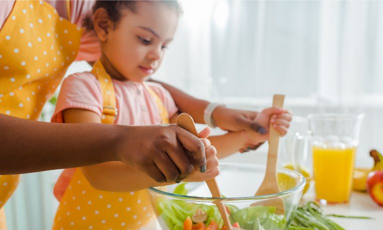 Young girl tossing salad with mom