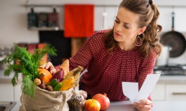 Young woman checking bag of produce, on her kitchen counter, sales receipt in hand