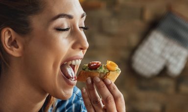 Closeup of young woman, eyes closed, mouth open, bringing piece of bruschetta in for a bite
