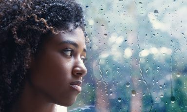 Young woman looking out through rain covered window, depressed